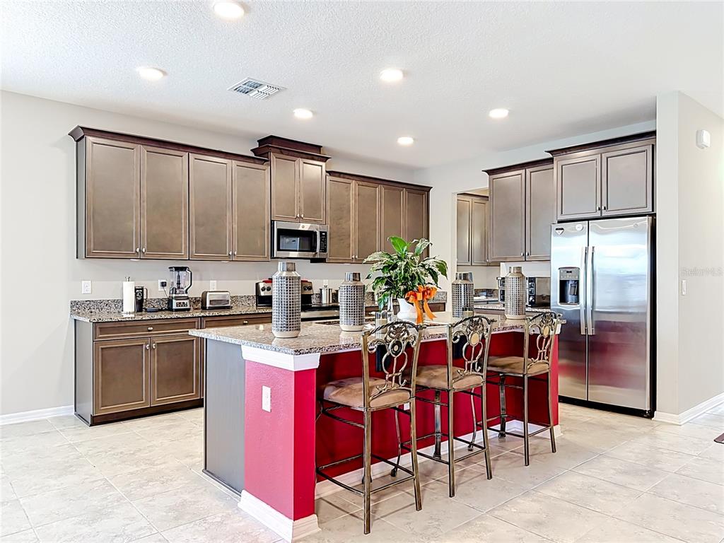 A kitchen features dark wood cabinets, granite countertops, a red island, and stainless steel appliances — 4923 EAGLE ROCK DRIVE, WIMAUMA, FL