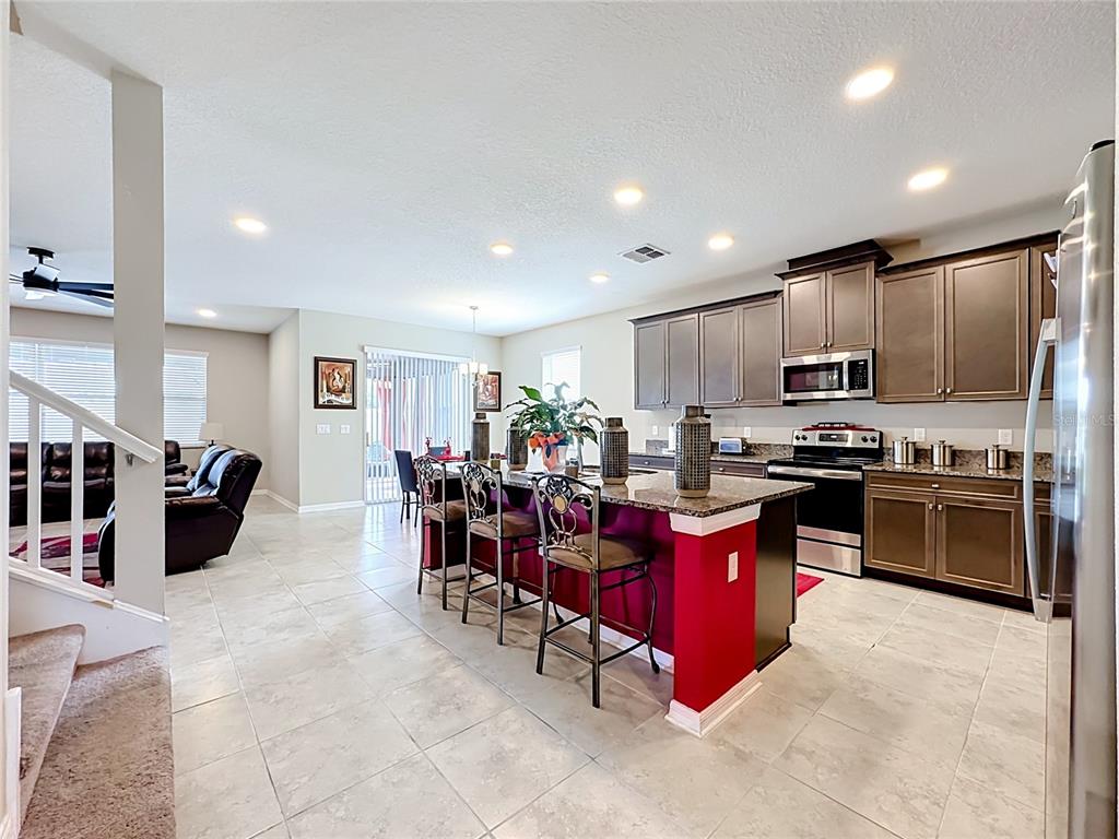 A kitchen with dark wood cabinets, granite countertops, and a red island with bar stools — 4923 EAGLE ROCK DRIVE, WIMAUMA, FL