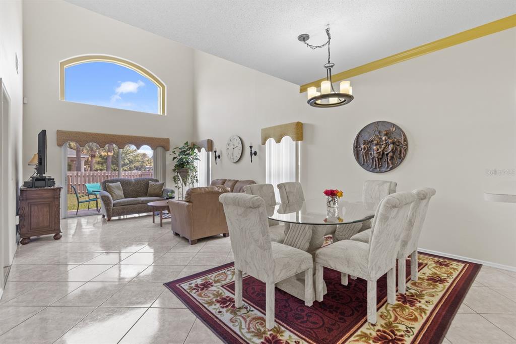 A dining and living area with high ceilings, tile floors, and a glass-topped dining table — 13037 LILY POND COURT, ORLANDO, FL