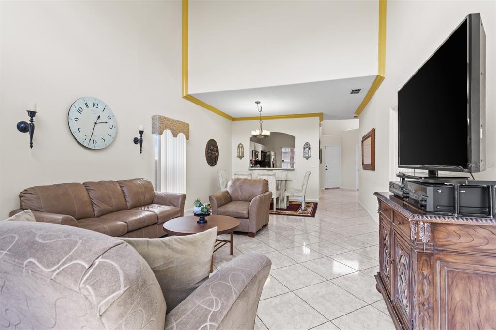 A living room with tile floors, leather furniture, a large wall clock, and a television — 13037 LILY POND COURT, ORLANDO, FL
