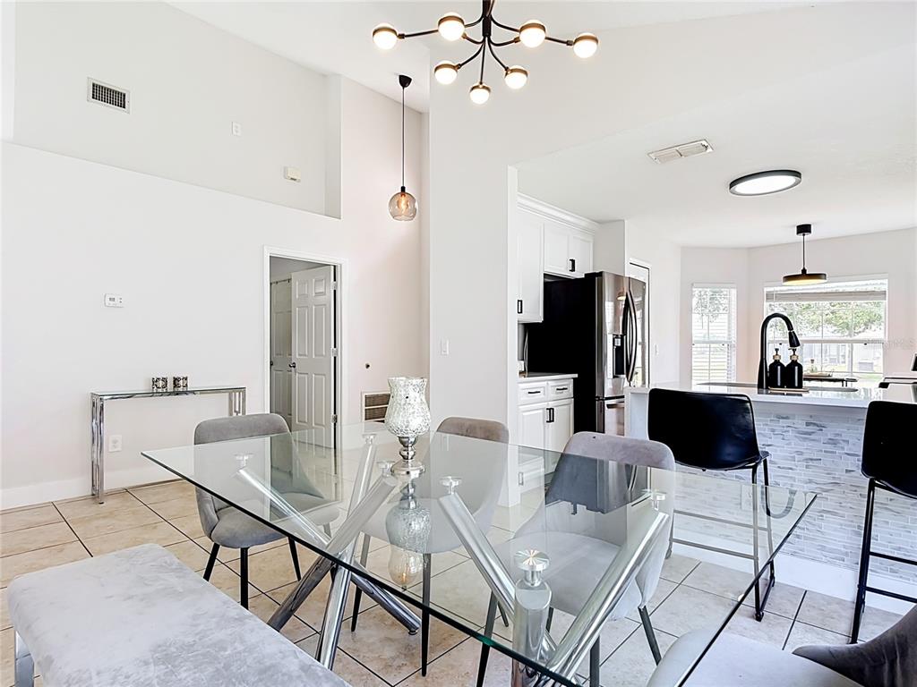A dining area with a glass table and bench sits adjacent to a white kitchen — 1021 TOURMALINE DRIVE, KISSIMMEE, FL