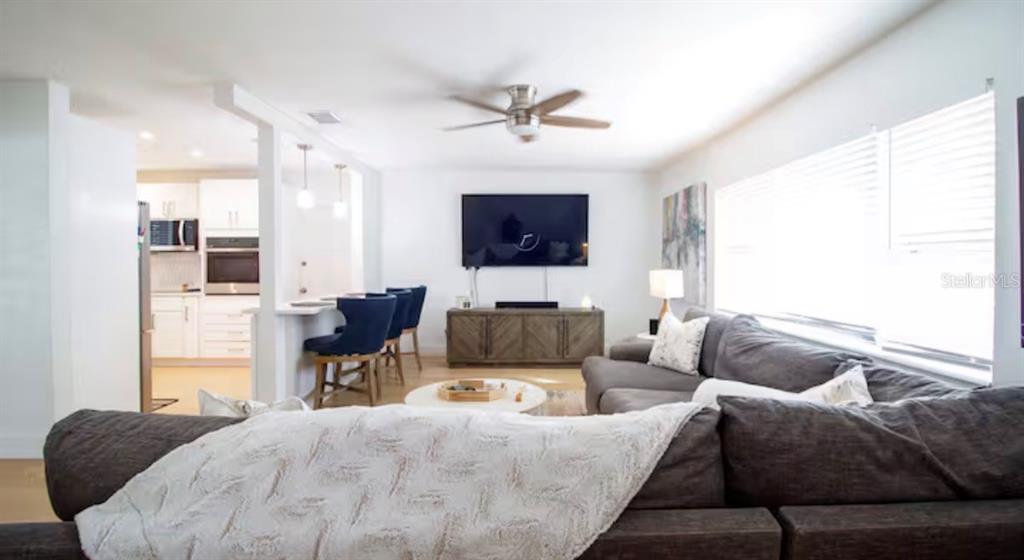 A living room with a sectional sofa, a wall-mounted television, and an adjacent kitchen area — 10541 86TH AVENUE, SEMINOLE, FL