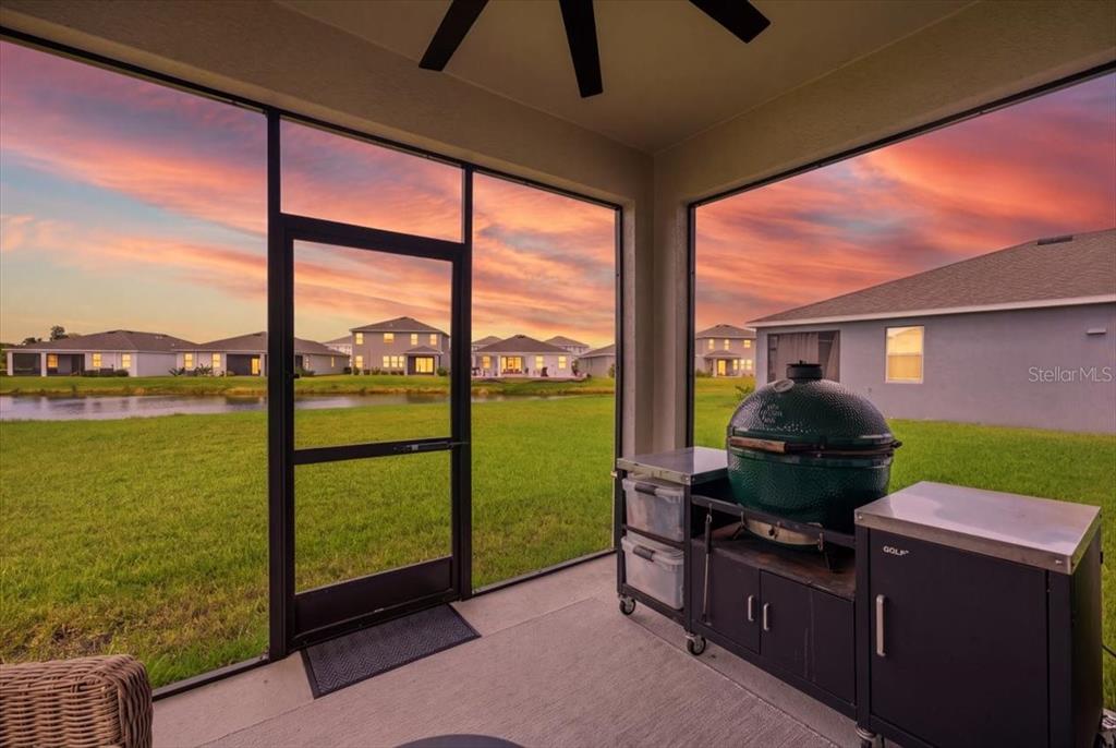 A screened-in patio features a green ceramic grill on a metal cart overlooking a pond — 16018 6TH AVENUE E, BRADENTON, FL