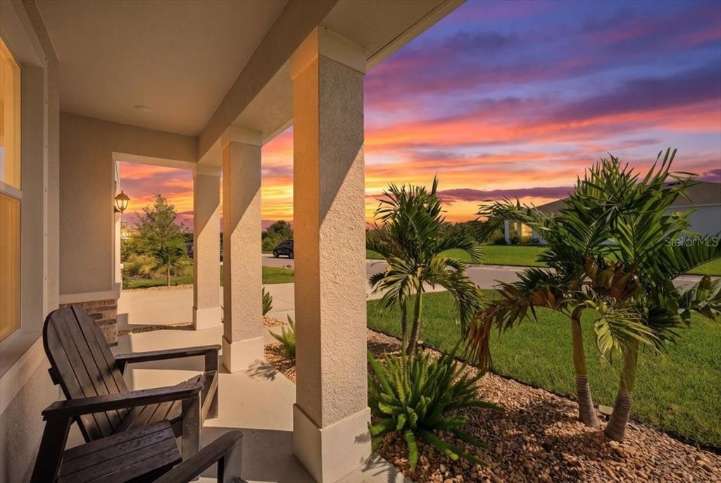 A covered front porch with a wooden chair overlooks a landscaped yard at sunset — 16018 6TH AVENUE E, BRADENTON, FL