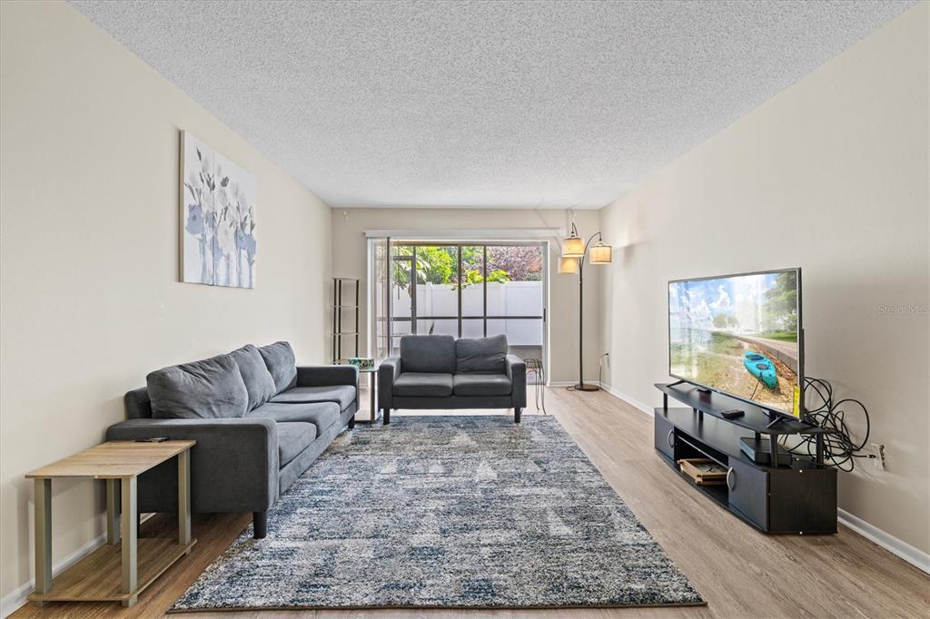 A living room features gray sofas, a patterned area rug, and a television on a stand — 3275 BENEVA ROAD UNIT 104, SARASOTA, FL