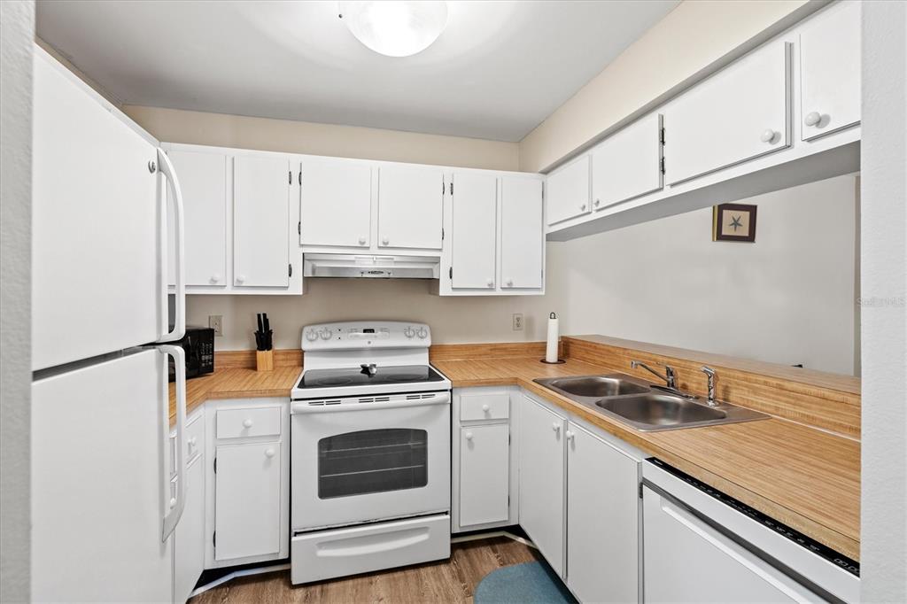 A kitchen features white cabinets, a white stove, a double sink, and wood-look countertops — 3275 BENEVA ROAD UNIT 104, SARASOTA, FL