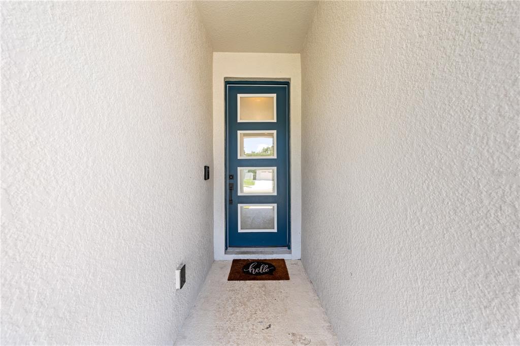 A blue front door with four glass panels sits at the end of a covered entryway — 4035 SOUTHERN VISTA LOOP, ST CLOUD, FL