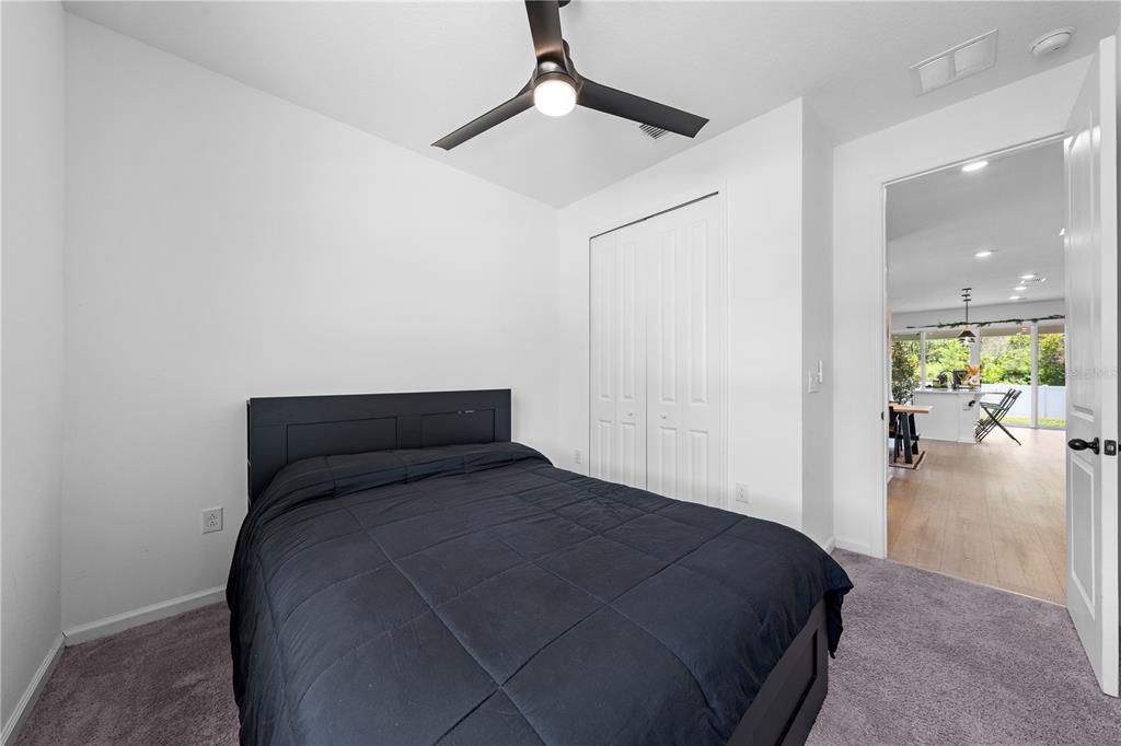 A bedroom with a black bed, ceiling fan, white walls, and a view into another room — 4035 SOUTHERN VISTA LOOP, ST CLOUD, FL