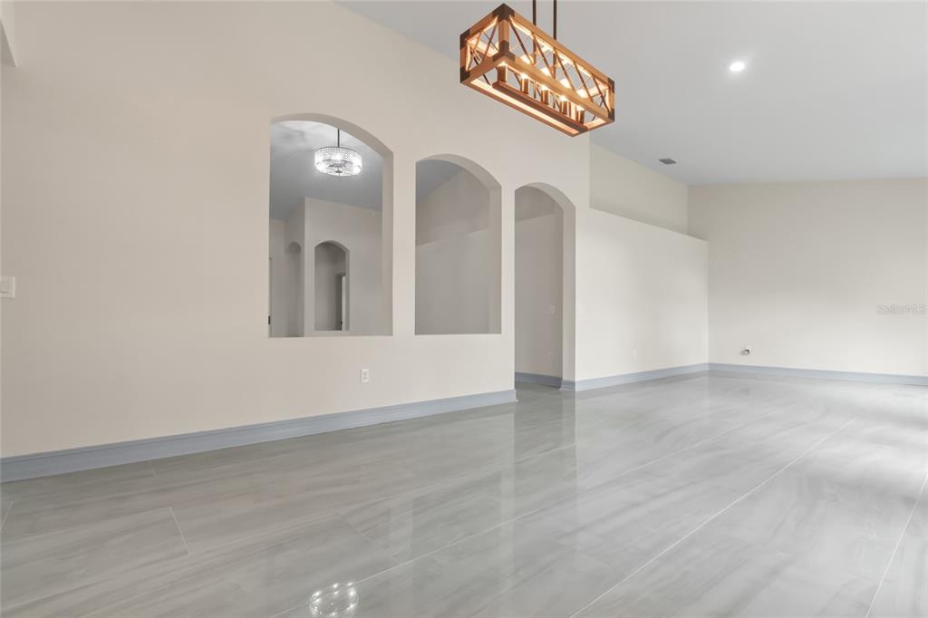 A room with gray tile flooring, arched wall cutouts, and a rectangular wooden chandelier — 10217 TIMBERLAND POINT DRIVE, TAMPA, FL