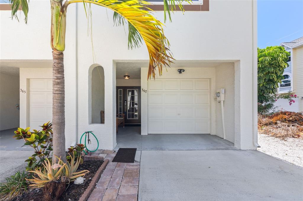 The exterior of a white townhouse features a garage, a front entrance, and a palm tree — 367 MADEIRA CIRCLE, TIERRA VERDE, FL