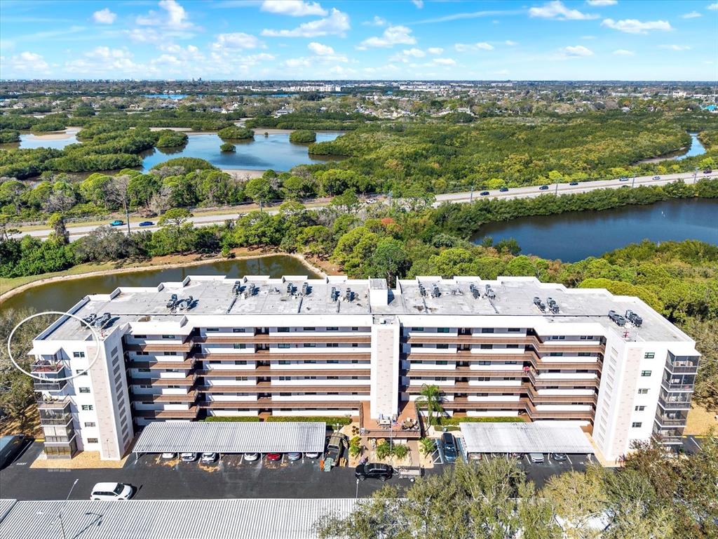 An aerial view shows a multi-story apartment building with covered parking and surrounding wetlands — 8186 TERRACE GARDEN DRIVE N UNIT 601, ST PETERSBURG, FL