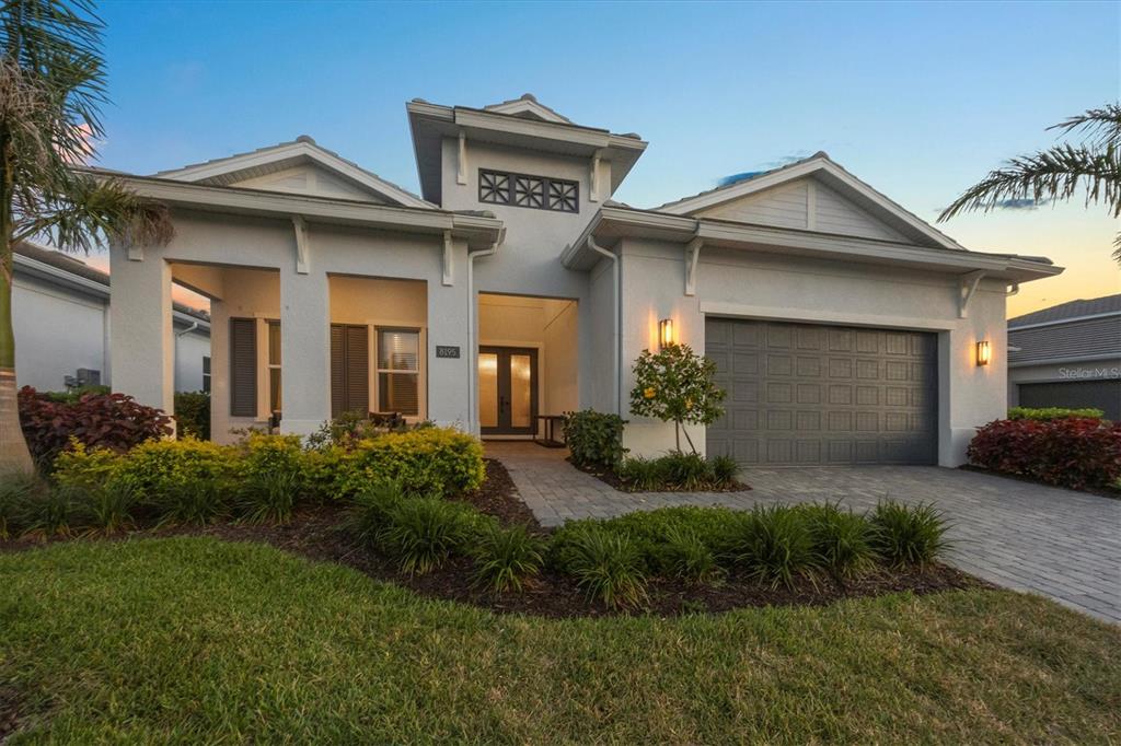 A single-story house with a gray garage, light-colored stucco exterior, and a paved walkway — 8195 REDONDA LOOP, LAKEWOOD RANCH, FL