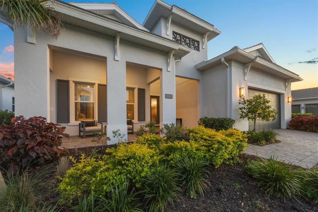 A single-story house exterior features a covered porch, gray shutters, and a paved driveway — 8195 REDONDA LOOP, LAKEWOOD RANCH, FL