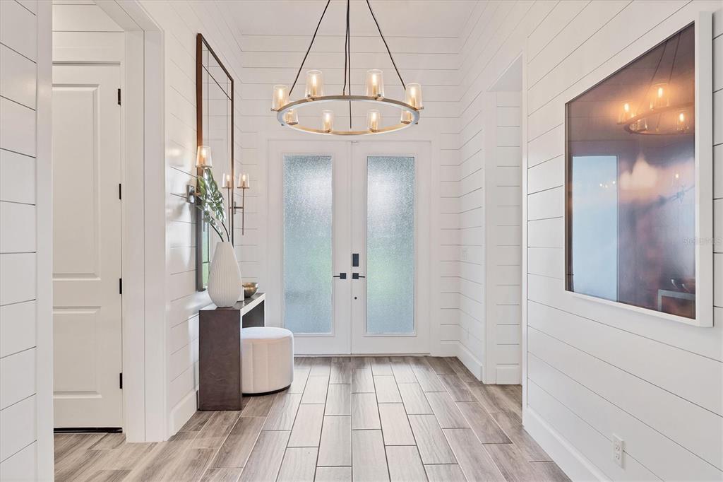 A bright entryway features white shiplap walls, a circular chandelier, and wood-look tile flooring — 8195 REDONDA LOOP, LAKEWOOD RANCH, FL