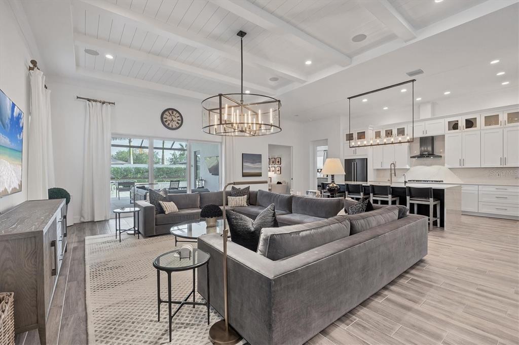 A spacious open-concept living room and kitchen featuring a large sectional sofa and coffered ceilings — 8195 REDONDA LOOP, LAKEWOOD RANCH, FL