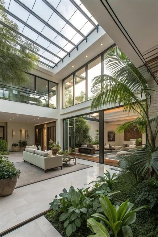 A modern living room with a glass atrium ceiling, indoor plants, and large floor-to-ceiling windows — 3181 GULF BOULEVARD, BELLEAIR BEACH, FL