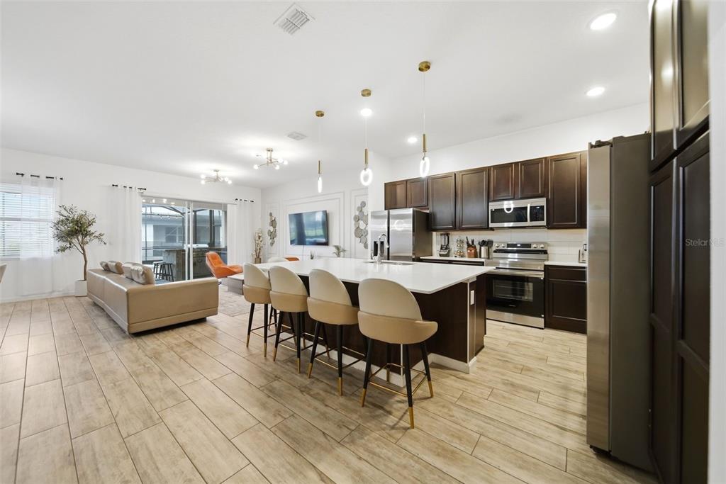 An open-concept kitchen and living area features dark wood cabinets, a white island, and tile flooring — 2532 SHANTI DRIVE, KISSIMMEE, FL