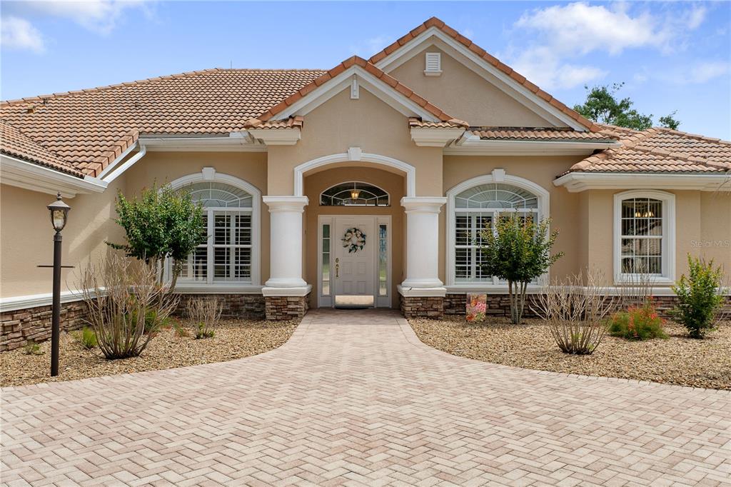 The exterior of a beige house features a tiled roof, stone accents, and a paved walkway — 1969 N YAWKEY POINT, HERNANDO, FL