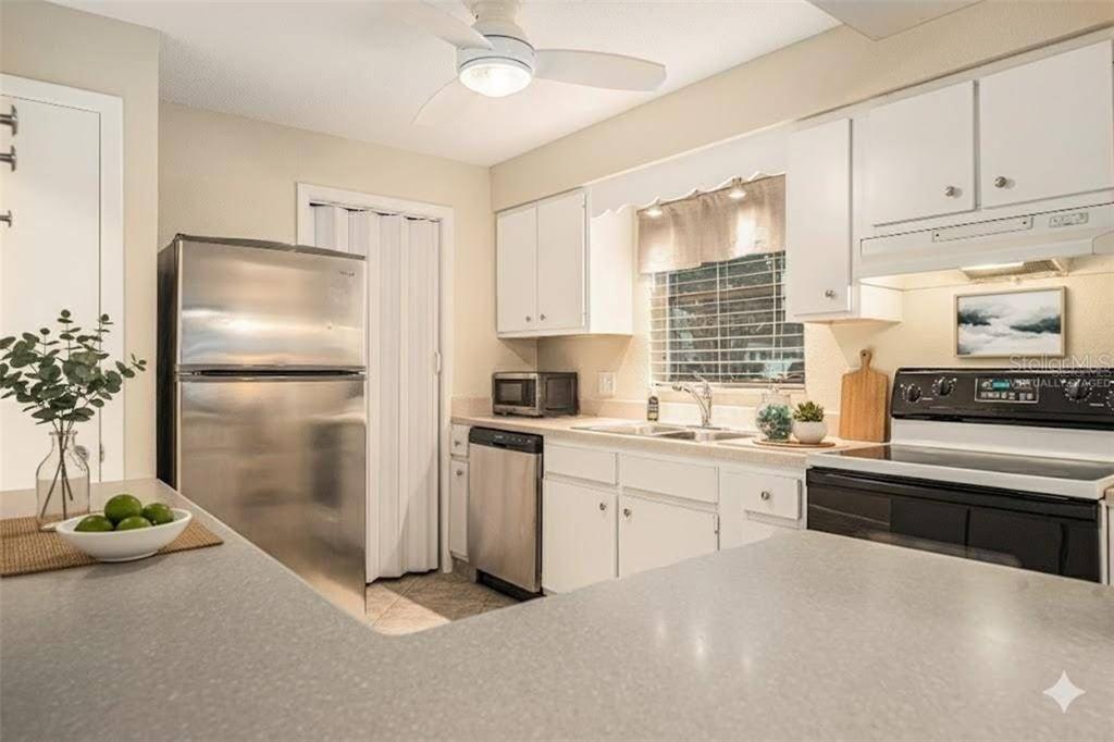 A kitchen features white cabinets, stainless steel appliances, and a gray countertop with a breakfast bar — 11200 102ND AVENUE UNIT 16, SEMINOLE, FL