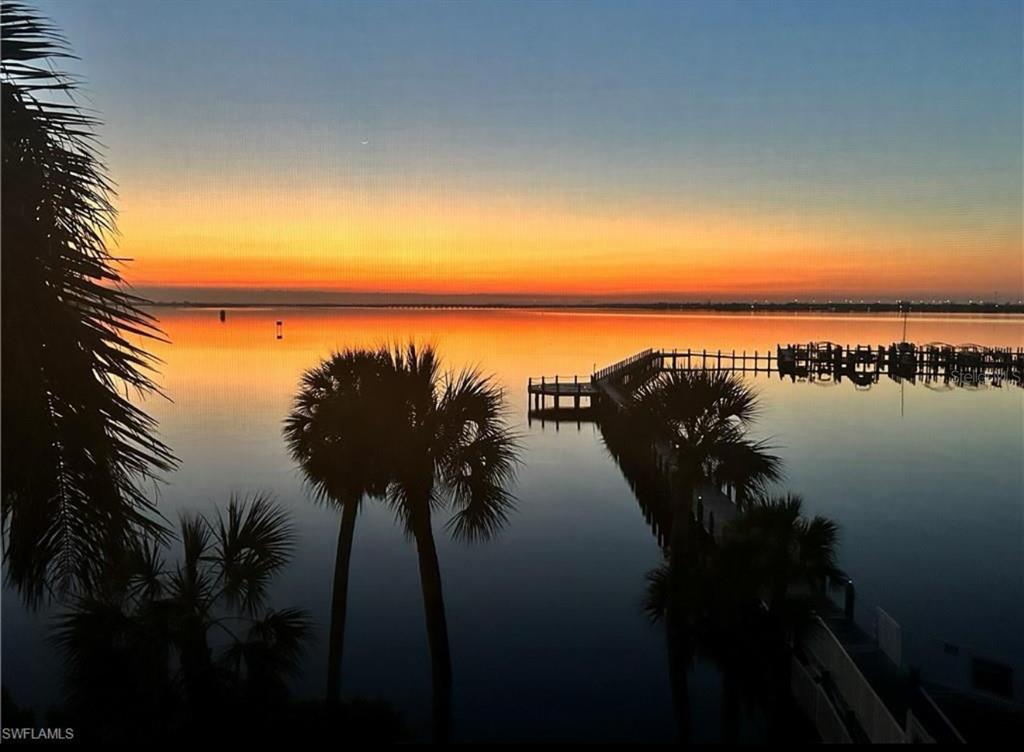 A sunset view over a calm body of water featuring a wooden pier and palm trees — 5114 MELBOURNE STREET UNIT A302, PUNTA GORDA, FL