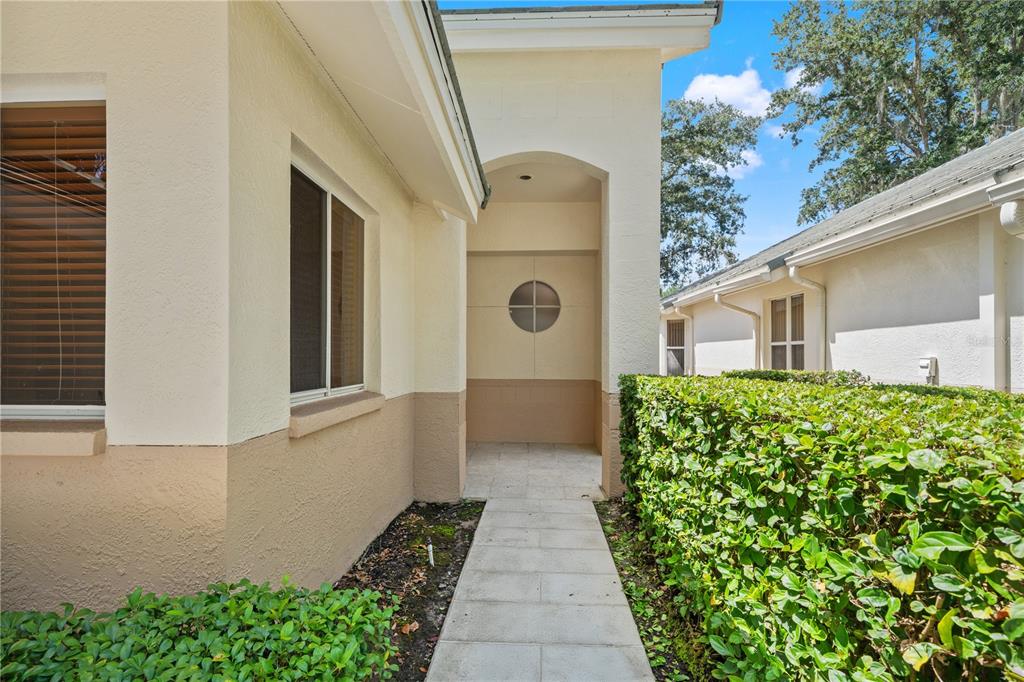 A paved walkway leads to a recessed entryway featuring a circular window on the wall — 6005 FAIRWAY PALMS COURT, TAMPA, FL