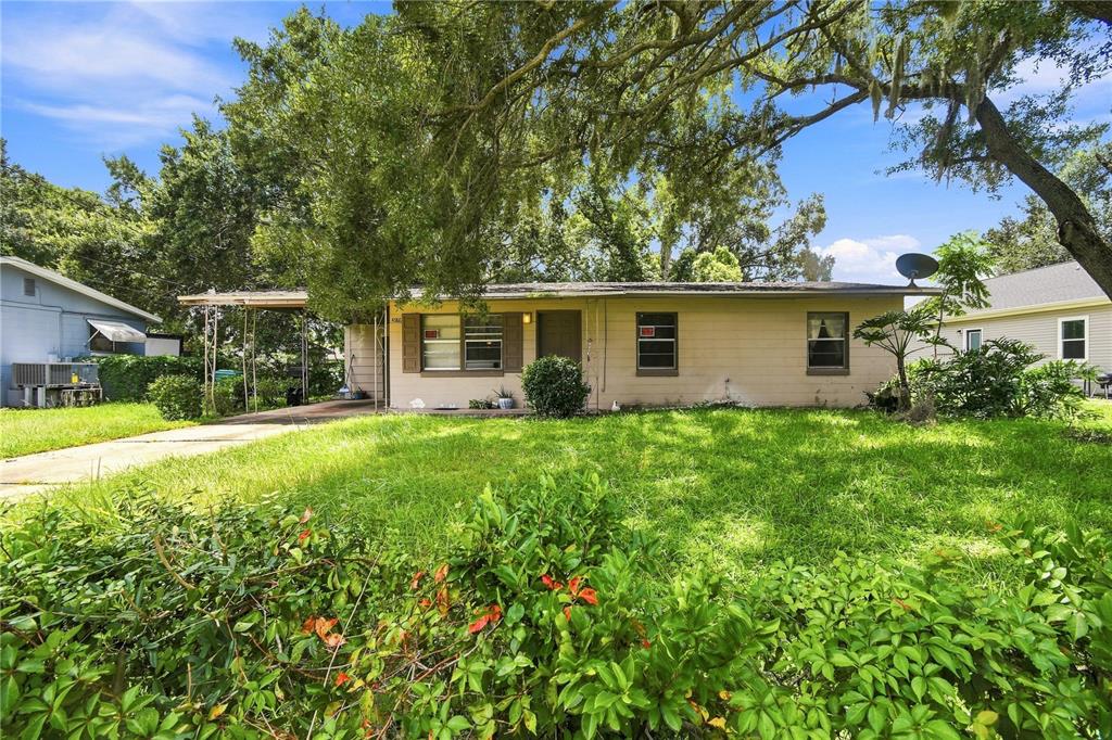 A single-story tan house with a carport and a large front lawn under mature trees — 4186 CEPEDA STREET, ORLANDO, FL
