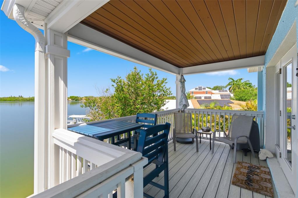 A covered balcony features blue high-top chairs and a table overlooking a waterfront view — 4805 COBIA DRIVE SE UNIT D Furnished, ST PETERSBURG, FL