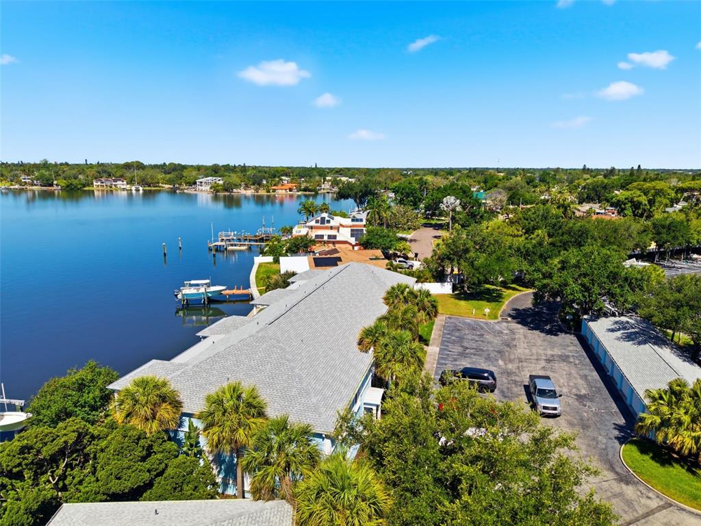 An aerial view shows a waterfront building with a gray roof, parking lot, and docks — 4805 COBIA DRIVE SE UNIT D Furnished, ST PETERSBURG, FL