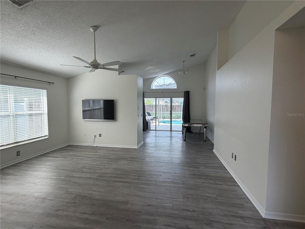 A living room with gray wood-look flooring, a ceiling fan, wall-mounted television, and sliding glass doors — 314 ALLISON AVENUE, DAVENPORT, FL