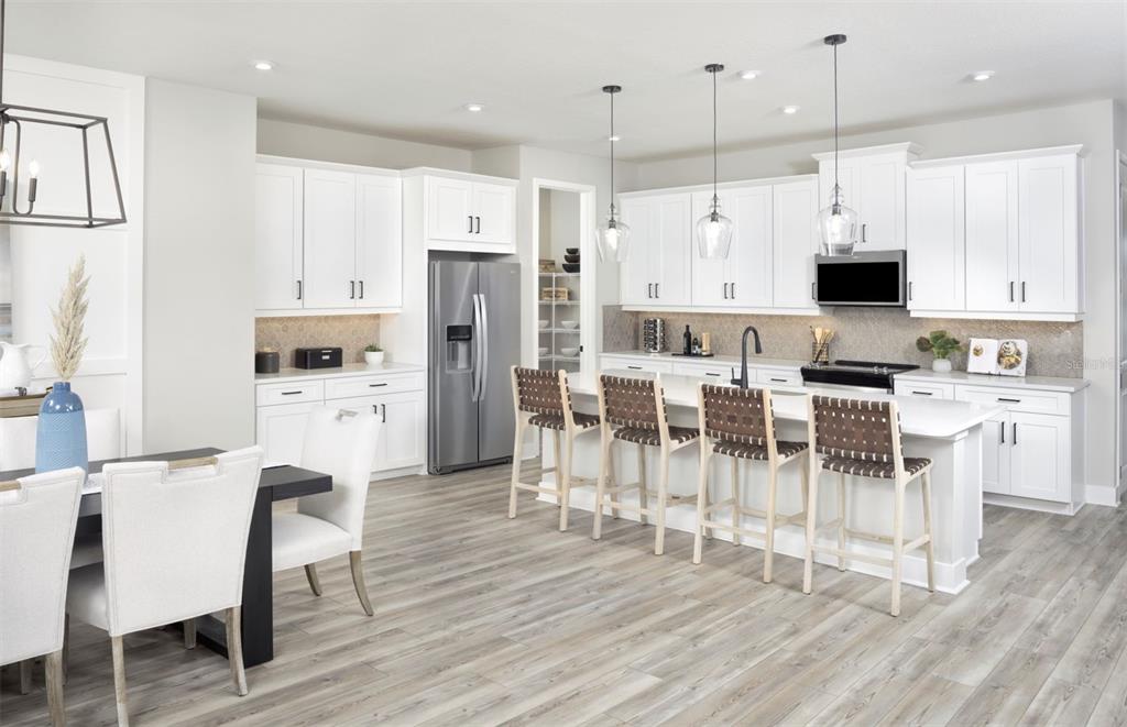 A modern kitchen features white cabinetry, a large island with bar seating, and wood-look flooring — 35507 PEAK WILLOW TRACE, DADE CITY, FL