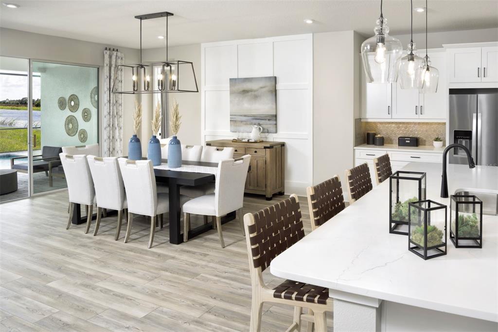 An open-concept dining area and kitchen feature white cabinetry, a dark dining table, and island seating — 35507 PEAK WILLOW TRACE, DADE CITY, FL