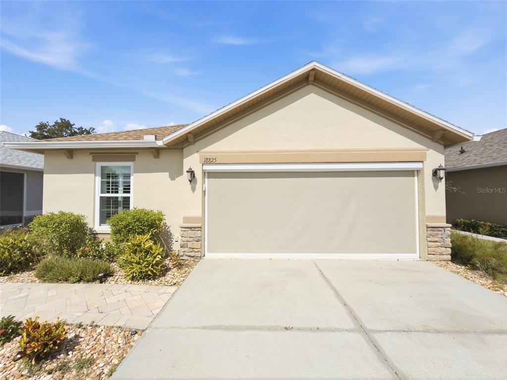 A single-story house exterior features a beige stucco facade, a two-car garage, and landscaping — 18825 WATER LILY LANE, HUDSON, FL