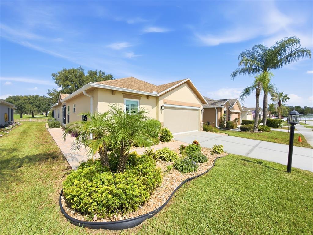 A tan single-story house with a two-car garage and a landscaped front yard — 18825 WATER LILY LANE, HUDSON, FL