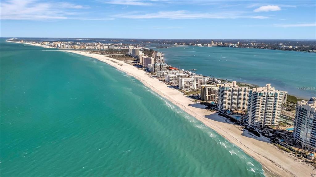 An aerial view shows high-rise condominiums along a sandy beach bordering the turquoise ocean — 1230 GULF BOULEVARD UNIT 403, CLEARWATER BEACH, FL