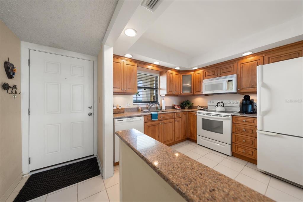 A kitchen with wood cabinets, granite countertops, white appliances, and a tiled floor — 1230 GULF BOULEVARD UNIT 403, CLEARWATER BEACH, FL