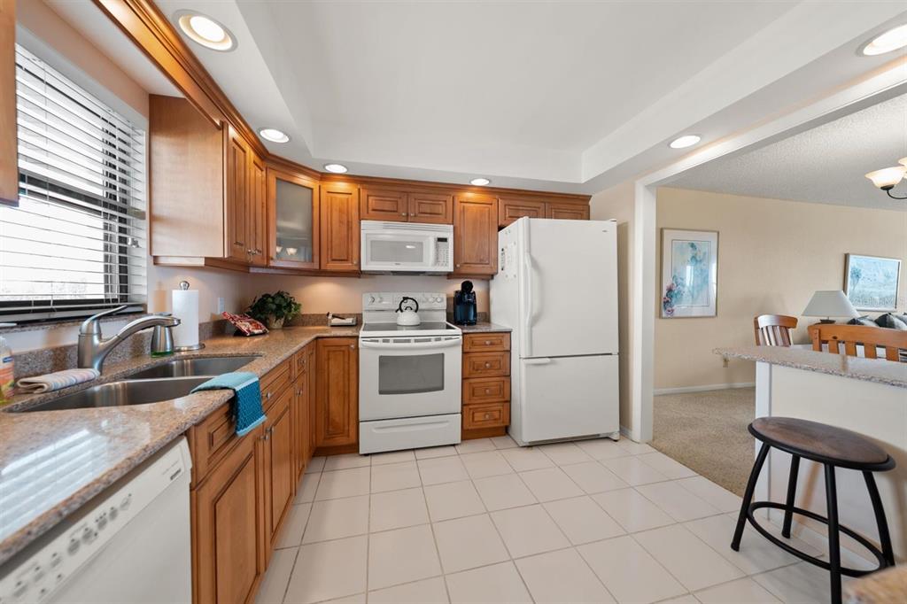 A kitchen features wooden cabinets, white appliances, granite countertops, and tile flooring — 1230 GULF BOULEVARD UNIT 403, CLEARWATER BEACH, FL