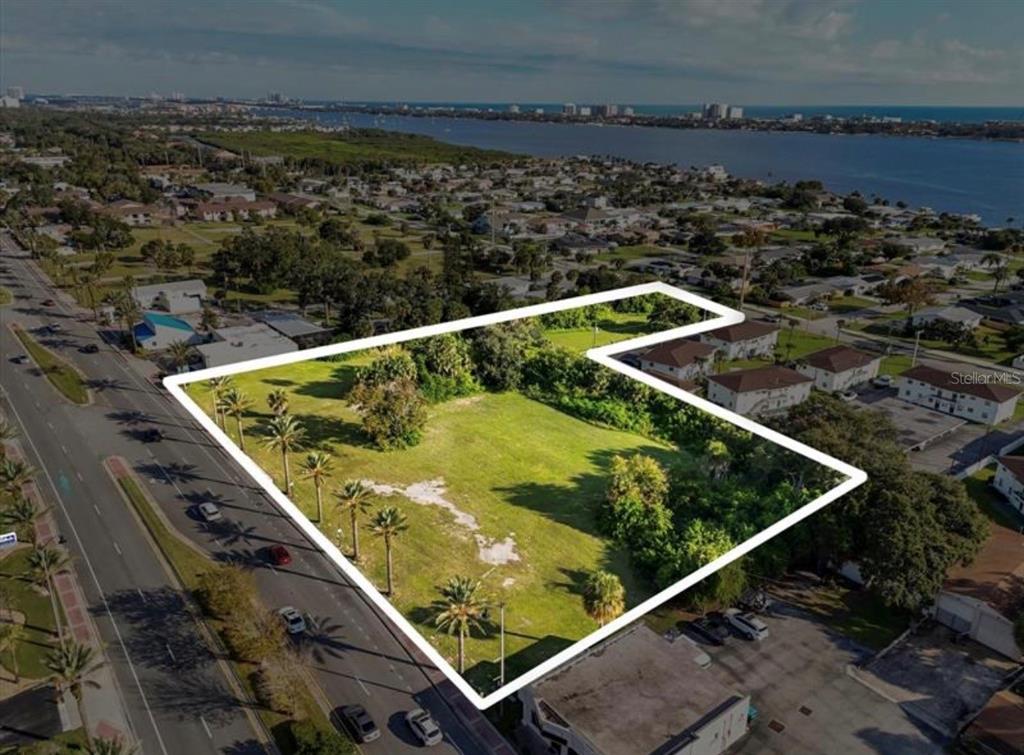 An aerial view shows a vacant, L-shaped grassy lot outlined in white along a road — 1745 S RIDGEWOOD AVENUE, SOUTH DAYTONA, FL