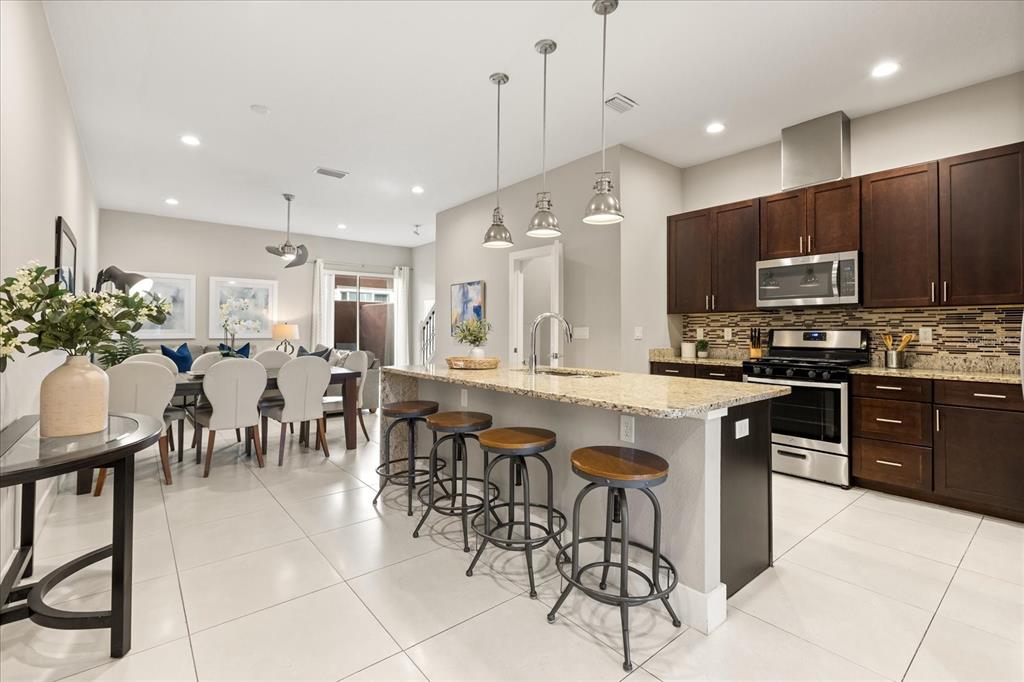 A kitchen with dark wood cabinets, granite countertops, and a breakfast bar with four stools — 2637 SUNRISE SHORES DRIVE, KISSIMMEE, FL