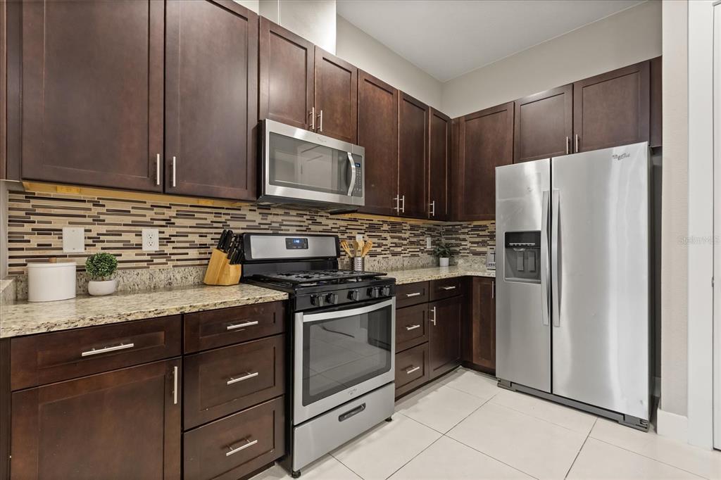 A kitchen with dark wood cabinets, stainless steel appliances, granite countertops, and a tiled backsplash — 2637 SUNRISE SHORES DRIVE, KISSIMMEE, FL
