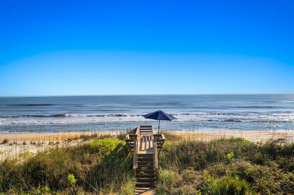 A wooden staircase leads through sand dunes to a beach with a blue umbrella — 11 OCEAN DUNE CIRCLE, PALM COAST, FL