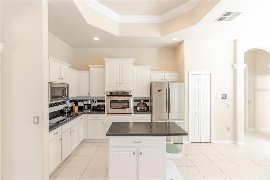 A kitchen with white cabinets, stainless steel appliances, a dark island, and tile flooring — 13382 SAGEWATER COURT, SPRING HILL, FL