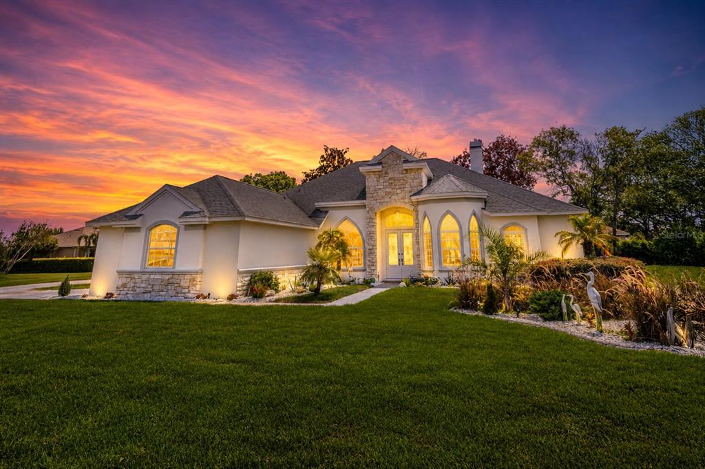 A single-story house with a stone facade and arched windows at sunset — 13382 SAGEWATER COURT, SPRING HILL, FL