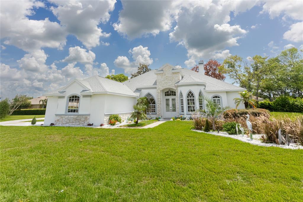 A white single-story house with stone accents, arched windows, and a large front lawn — 13382 SAGEWATER COURT, SPRING HILL, FL