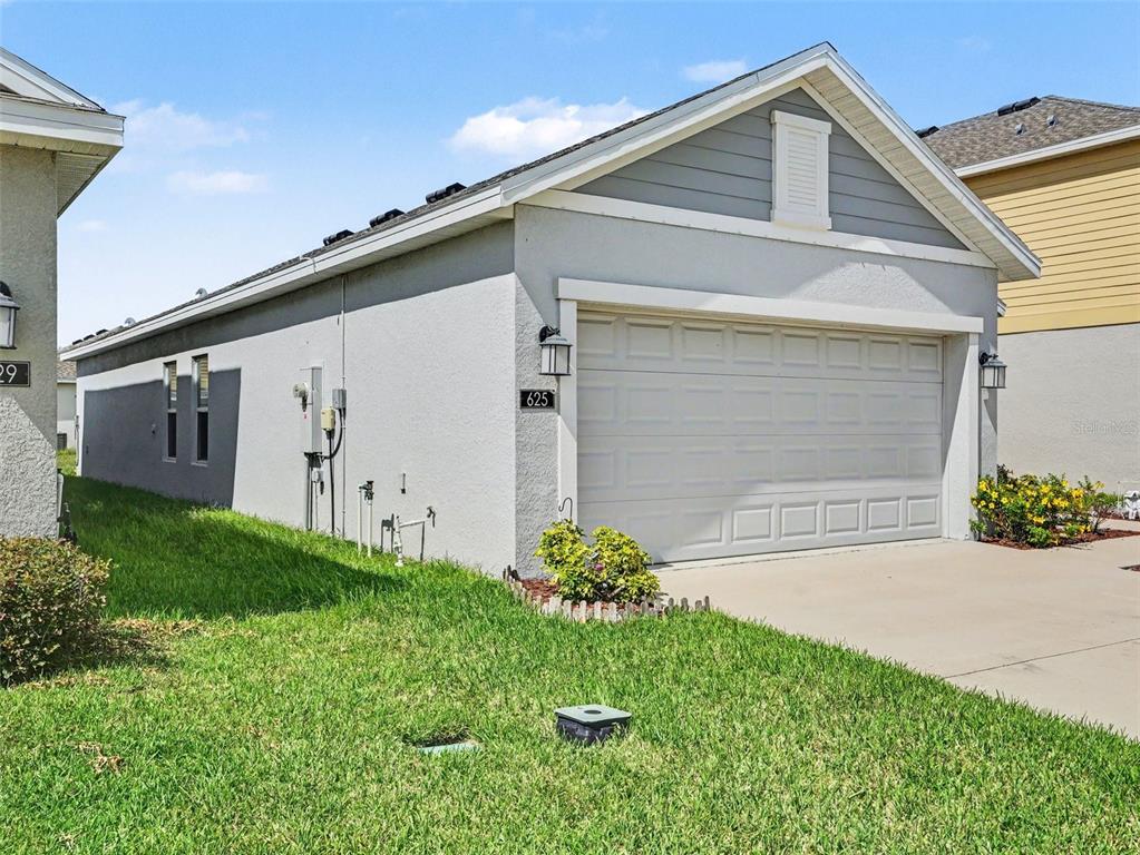 A side view of a single-story house exterior featuring a garage and a grassy yard — 625 TROTTERS DRIVE, EAGLE LAKE, FL