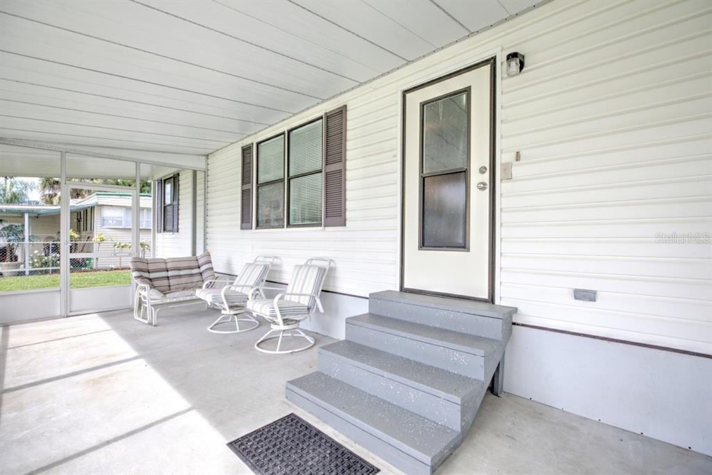 A covered porch with gray steps, outdoor furniture, and white siding leads to a door — 3523 SE 35TH AVENUE, OKEECHOBEE, FL