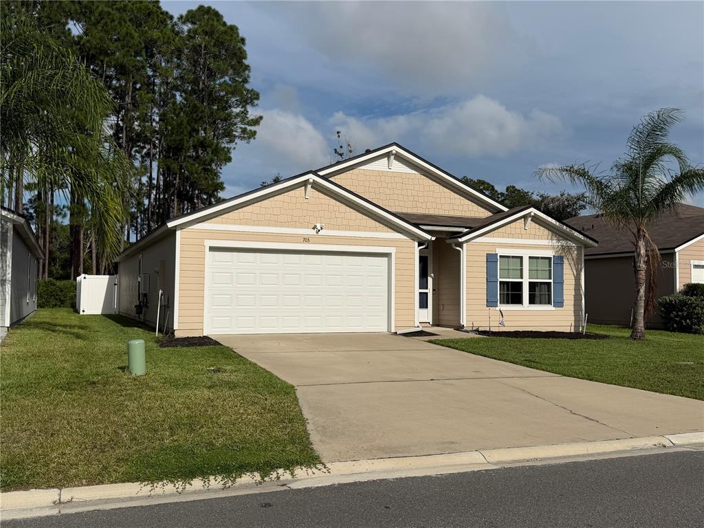 A single-story house with tan siding, a two-car garage, and a palm tree in front — 703 GRAND RESERVE DRIVE, BUNNELL, FL