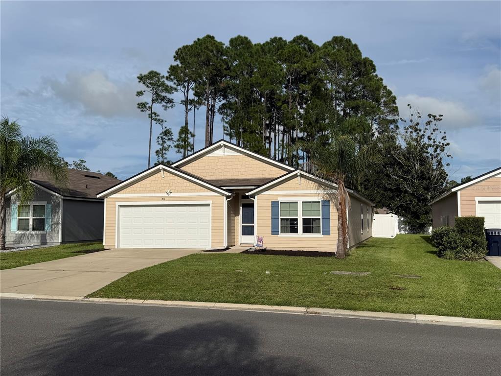 A single-story tan house with a two-car garage and blue shutters sits under a blue sky — 703 GRAND RESERVE DRIVE, BUNNELL, FL