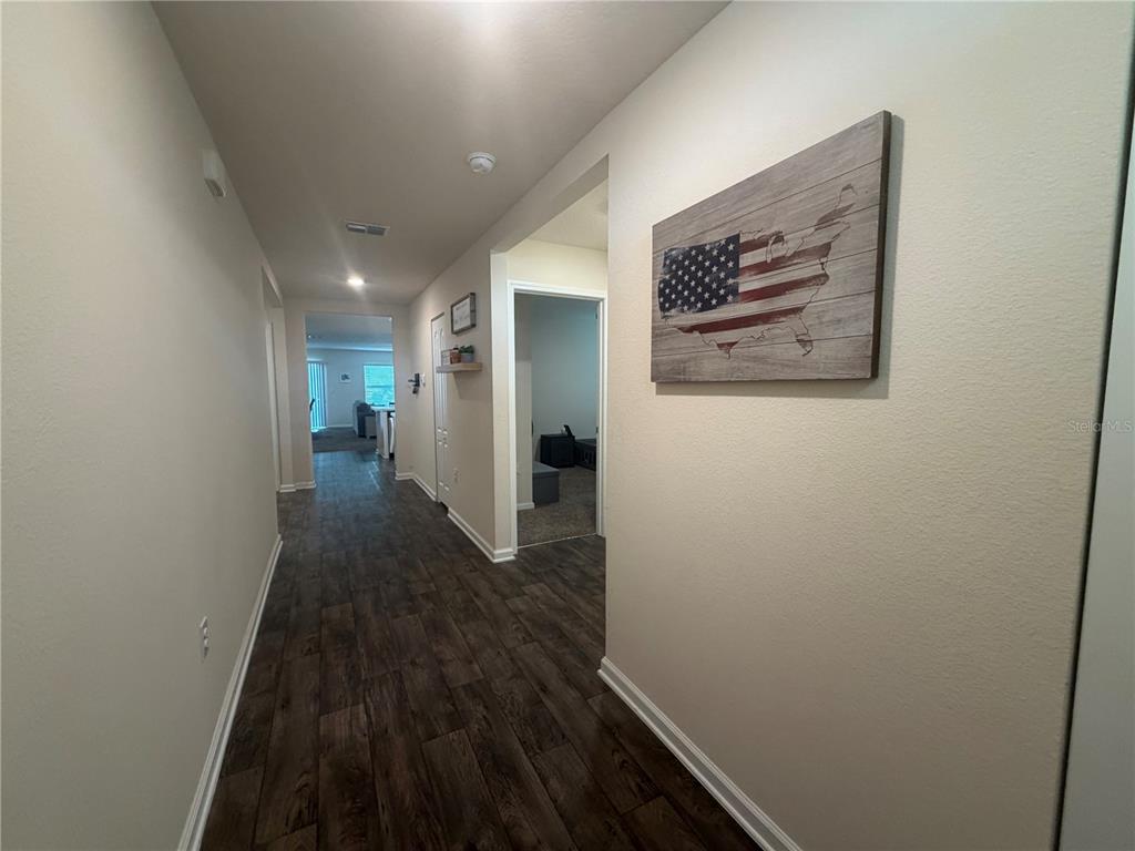 A hallway with wood-look flooring leads to an open living area past a wall-mounted flag — 703 GRAND RESERVE DRIVE, BUNNELL, FL