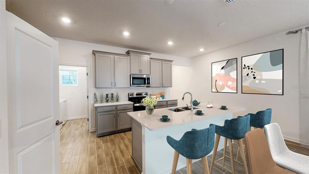 A kitchen features gray cabinets, a white island with bar stools, and wood-look tile flooring — 5654 KETTLEBELL ALLEY, CLERMONT, FL