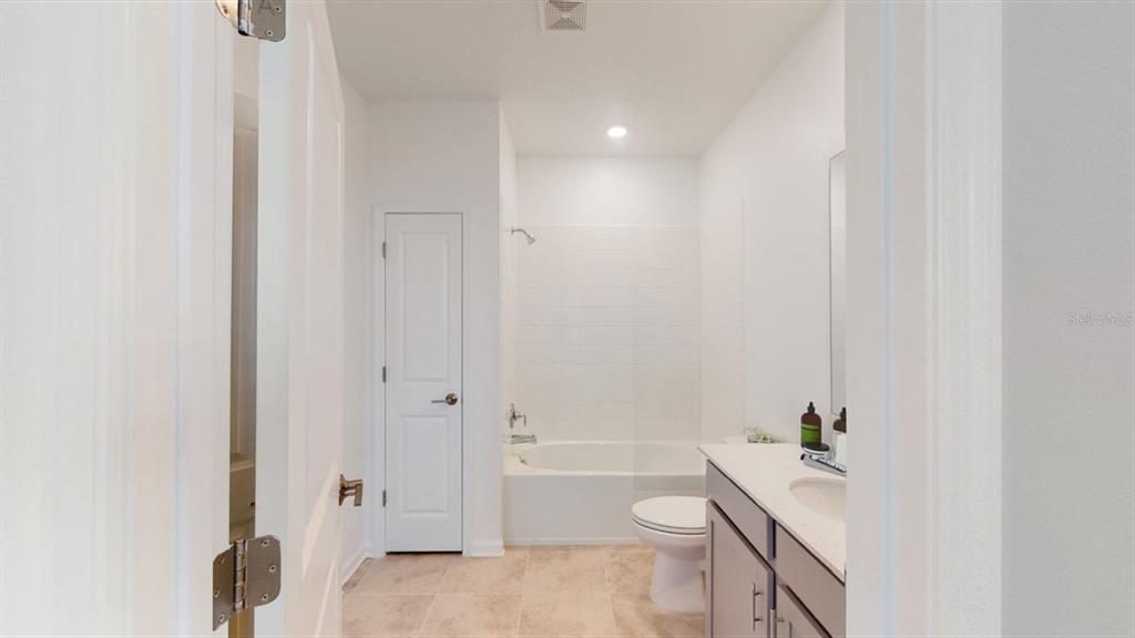 A bathroom features a white bathtub, a toilet, and a gray vanity with a sink — 5654 KETTLEBELL ALLEY, CLERMONT, FL